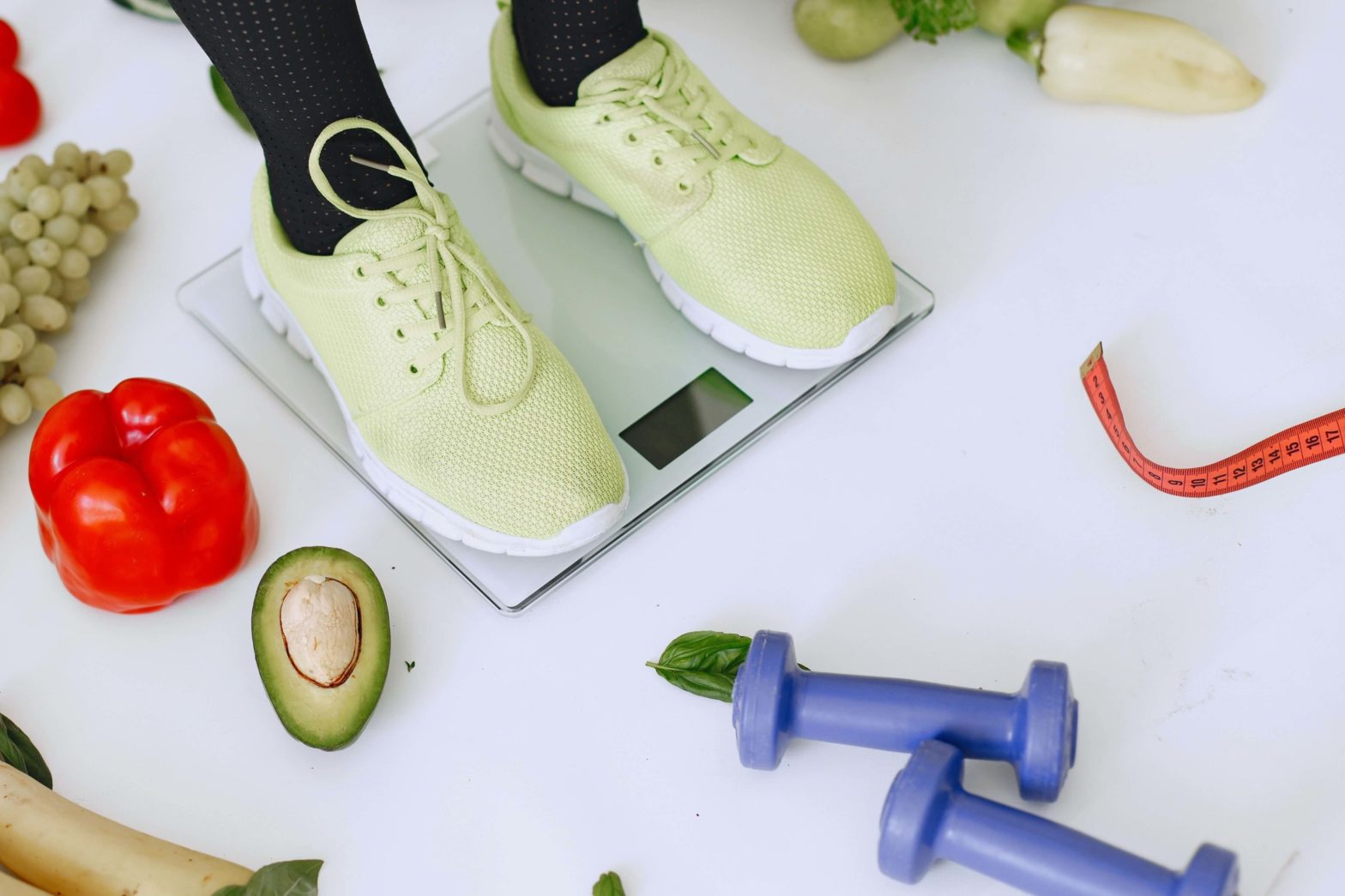 Woman's feet on scales surrounded by fruit and veggies.